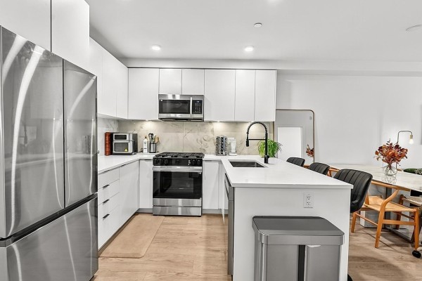 Modern kitchen with white cabinets, stainless steel appliances, and island. - 421 13238 105 Avenue, Surrey