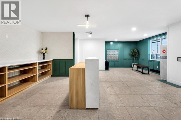 Modern apartment building lobby with a reception desk, wood shelving, and teal accent wall. - 421 Fairview Drive Unit# 503, Brantford