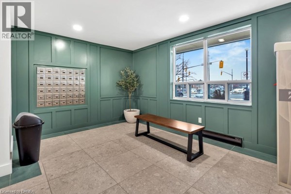 Apartment building lobby with mailboxes, a bench, a plant, and a window overlooking the street. - 421 Fairview Drive Unit# 503, Brantford