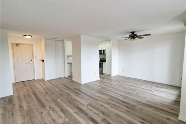 Open-concept living space with laminate flooring, white walls, a ceiling fan, and hallway leading to kitchen. - 421 Fairview Drive Unit# 503, Brantford