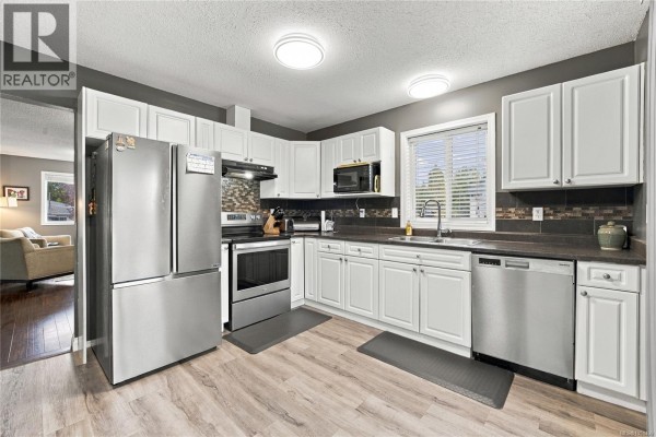 White kitchen with stainless steel appliances, a dishwasher, and a double-door refrigerator. - 421 Murray St, Nanaimo