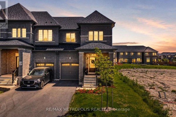 Exterior front view of a grey brick townhouse at dusk with illuminated windows and garage. - 421 Trevor Street, Cobourg