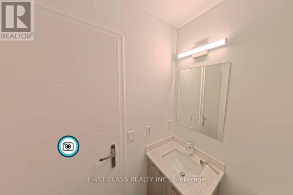 A bathroom vanity with a white sink, light wood cabinets, and a modern light fixture. - 4211 - 30 Francis Street, Kitchener