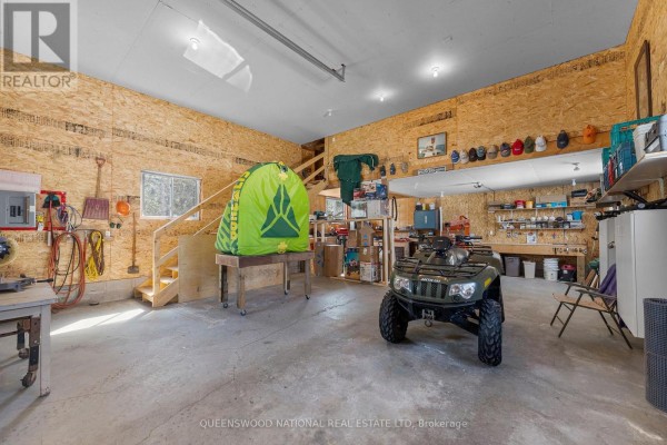 Spacious garage with OSB walls, concrete floor, workbench, and stairs - 42125 Combermere Road Ne, Madawaska Valley