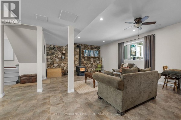 Finished basement living room with wood stove, stone accent wall, tile floors - 42125 Combermere Road Ne, Madawaska Valley