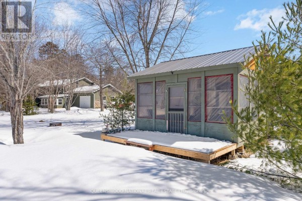 Green outbuilding with metal roof, wooden deck, snow; main house in background - 42125 Combermere Road Ne, Madawaska Valley
