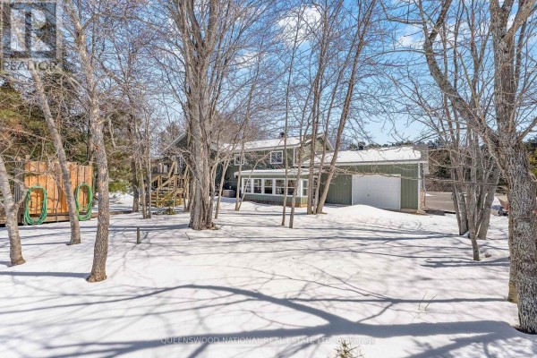 Green house with white garage, large windows, exterior stairs, snow, trees - 42125 Combermere Road Ne, Madawaska Valley