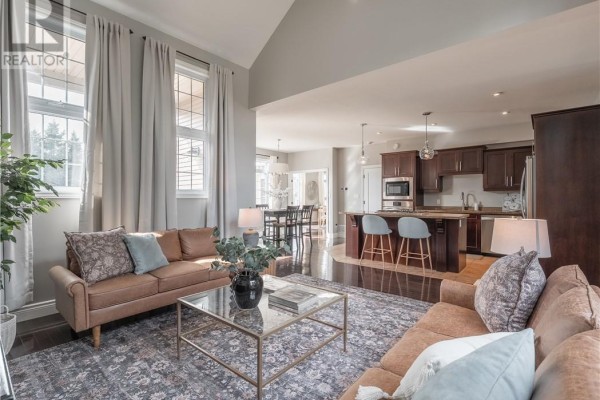 Living room with vaulted ceiling, tan sofas, patterned rug, and open view to kitchen. - 4215 Heritage Drive, Hanmer