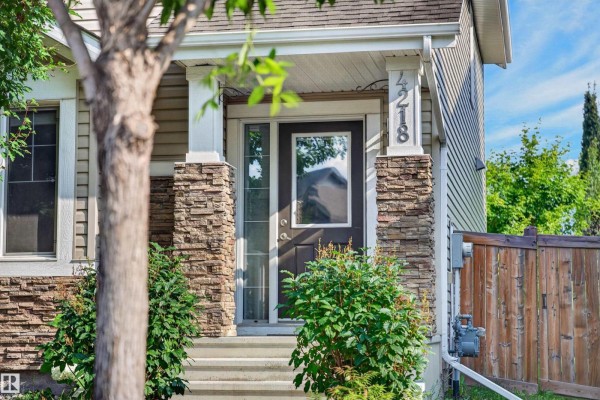 Front door with glass panel and stone pillars, surrounded by greenery. - 4218 Alexander Bay Sw, Edmonton