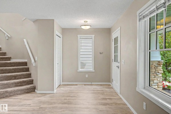 Interior entryway with a white door, staircase, and neutral-colored walls and floor. - 4218 Allan Li Sw, Edmonton