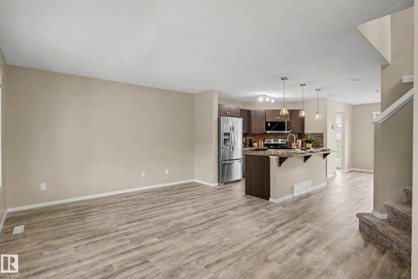 Living room and kitchen area with beige walls, wood-look flooring, and dark wood cabinets. - 4218 Allan Li Sw, Edmonton