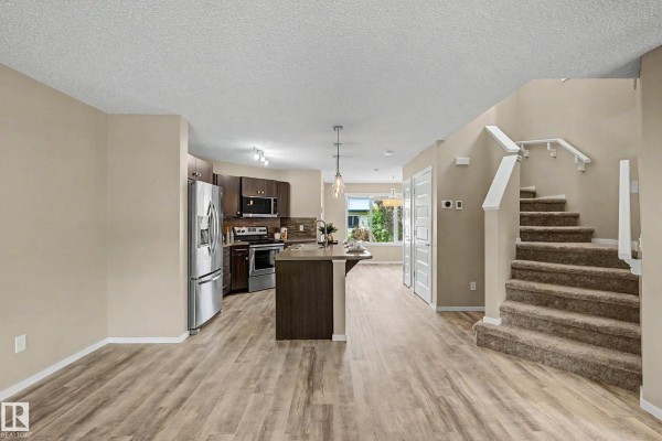 Open-concept living area and kitchen with a staircase leading upstairs and natural light. - 4218 Allan Li Sw, Edmonton