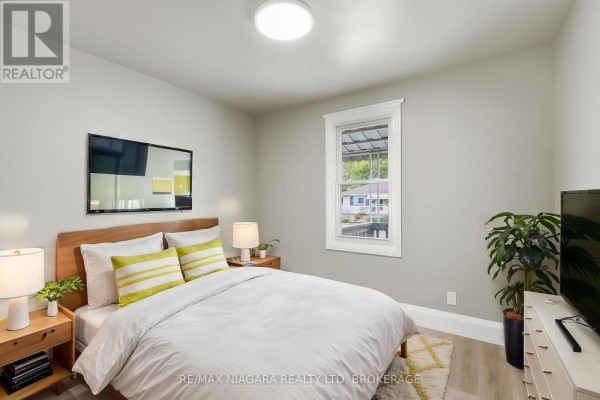 Bedroom with a wooden bed, two nightstands, a TV, and a window. - 422 Brunswick Street, Hamilton