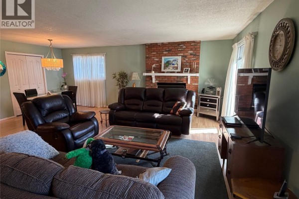 Living room with dark leather furniture, a brick fireplace, and a dining area with a chandelier. - 422 Manning Lane, Saskatoon