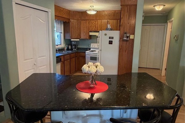Kitchen with light wood cabinets, white appliances, and a dark granite island with bar stools. - 422 Manning Lane, Saskatoon