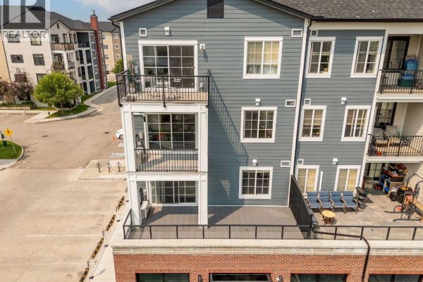 Aerial view of a grey apartment building with multiple balconies, brick base, and surrounding complex. - 4220, 215 Legacy Boulevard Se, Calgary