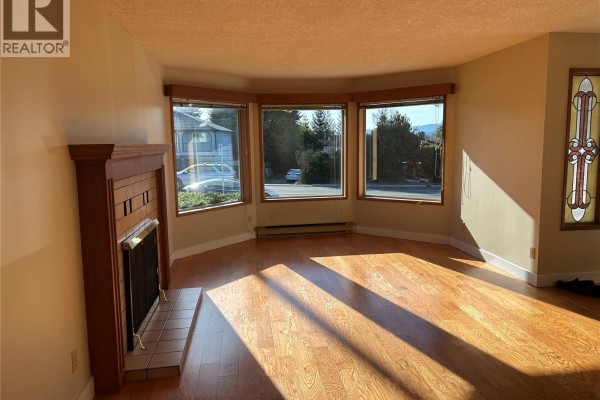 Living room with a fireplace, bay windows, and stained glass windows. - 4225 Quadra St, Saanich