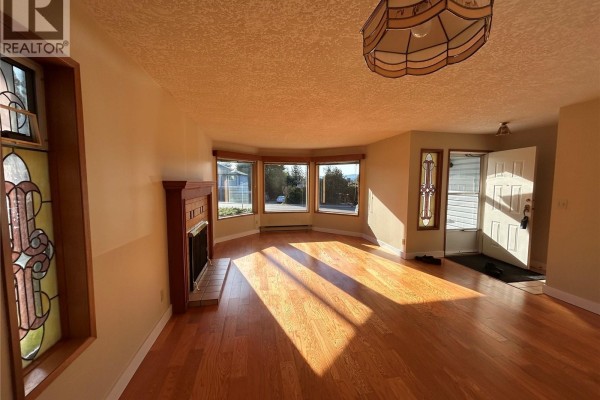 Interior view of a living room with a fireplace, bay windows, and the front entrance. - 4225 Quadra St, Saanich