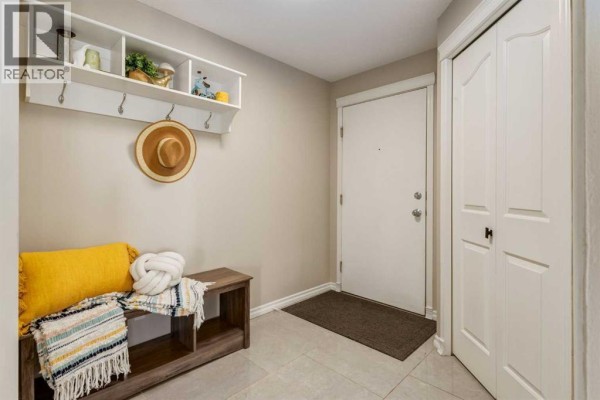 Apartment entryway with tiled floor, wooden bench, hat shelf, and white double doors. - 4226, 10 Prestwick Bay Se, Calgary