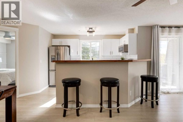Kitchen with white cabinetry, stainless steel appliances, and a breakfast bar with black stools. - 4226, 10 Prestwick Bay Se, Calgary