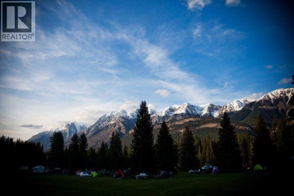 Tents and vehicles set up on a grassy field with forested mountains. - 4227-4233 Beaverfoot Forest Service Road, Golden