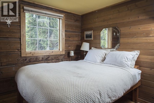 Bedroom with knotty pine walls, queen bed, and large window view. - 4227-4233 Beaverfoot Forest Service Road, Golden