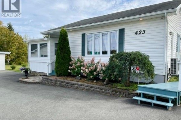 Side view of the white bungalow with a sunroom, deck, and air conditioning unit. - 423 Darlington, Dalhousie