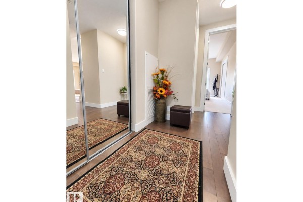 Entryway with a large mirrored closet door, a decorative rug, and two small dark brown ottomans. - #424 11074 Ellerslie Rd Sw, Edmonton