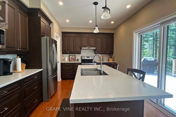 Front view of a beige house with a double garage, walkway, and trees. - 424 Lakewoods Drive, Madawaska Valley