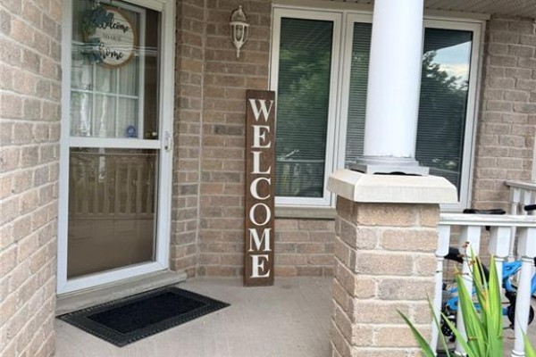 Close-up of the front door porch with a welcome sign, a screen door, and brick pillars. - 424 Newport Drive, Cambridge