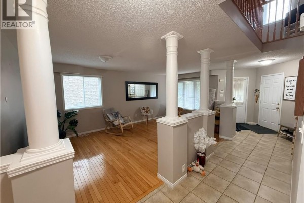 Open-concept living area with hardwood floors, decorative columns, a rocking chair, and a view of the entryway. - 424 Newport Drive, Cambridge