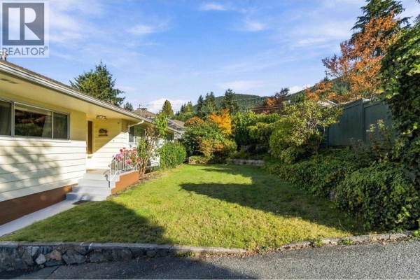 Side view of a cream-colored house with a grassy lawn and garden. - 4243 Delbrook Avenue, North Vancouver