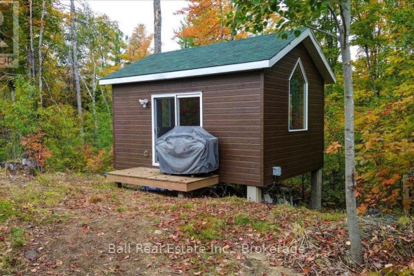 Side view of a small brown cabin with a green roof, set amongst trees with autumn foliage. - 4249 Old Hastings Road, Limerick