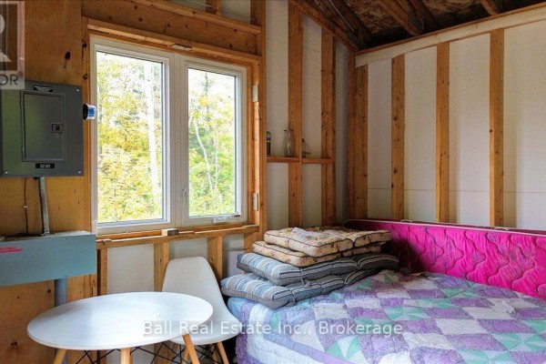 Interior view of a cabin showing a bed with patterned quilt, stack of cushions, small white table with chairs, and window. - 4249 Old Hastings Road, Limerick