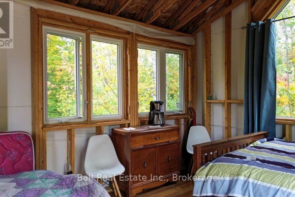 Interior of a cabin showing two beds, white chairs, a wooden dresser, and multiple windows looking out to trees. - 4249 Old Hastings Road, Limerick