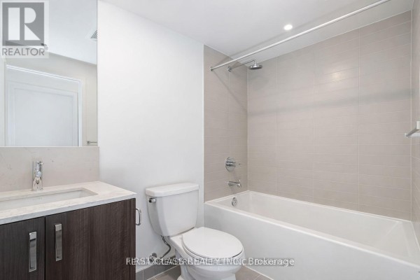 Apartment bathroom with a dark wood vanity, white toilet, and beige tiled tub. - 425 - 1787 St Clair Avenue W, Toronto