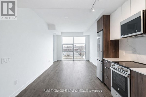 Open concept kitchen and living area with a large window, stainless steel appliances, and dark wood cabinets. - 425 - 1787 St Clair Avenue W, Toronto