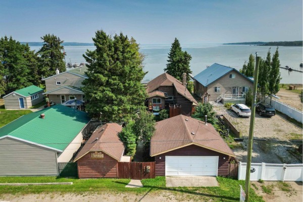 Aerial view of multiple houses and garages along a lake, with trees and water in the background. - 425 1 Av S, Rural Parkland County