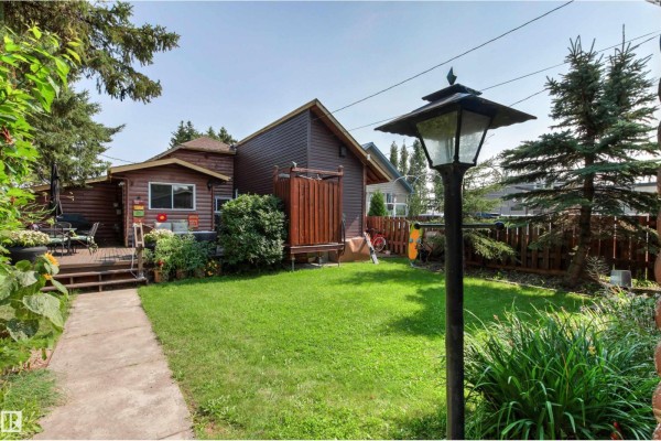 Backyard view of a brown wooden house with a green lawn, concrete pathway, and a lamp post. - 425 1 Av S, Rural Parkland County