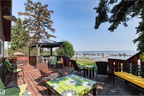 Wooden deck with outdoor furniture and a gazebo, overlooking a calm lake with a dock and boats. - 425 1 Av S, Rural Parkland County