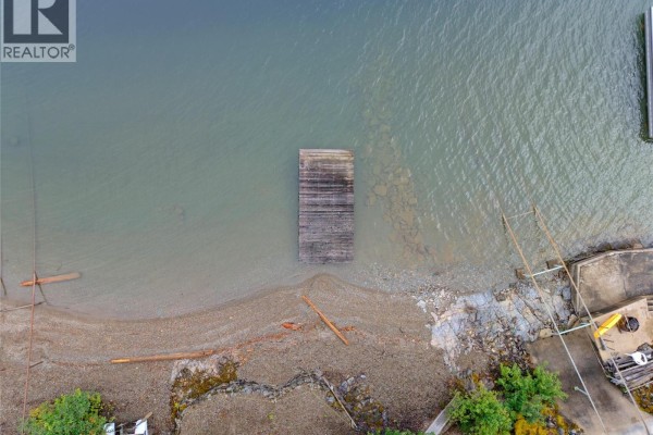 Overhead view of a wooden dock extending from a rocky shore into calm, greenish water. - 4255 Justin Road, Eagle Bay