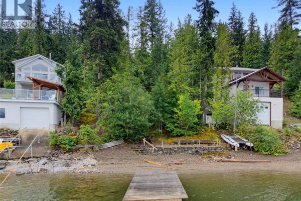 Waterfront view of two multi-story houses on a slope, with garages and balconies facing the lake. - 4255 Justin Road, Eagle Bay