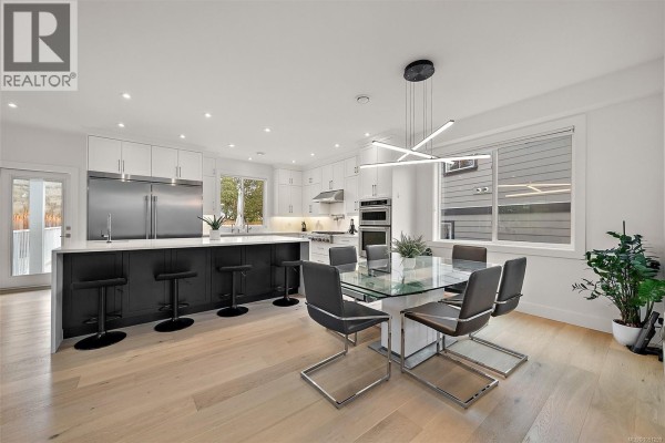 Dining area with glass table and modern chairs next to kitchen island and cabinets. - 4257 Pullet Pl, Saanich