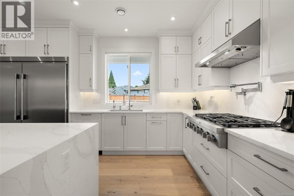 Modern kitchen with white cabinets, gas range, double ovens, and large island. - 4257 Pullet Pl, Saanich