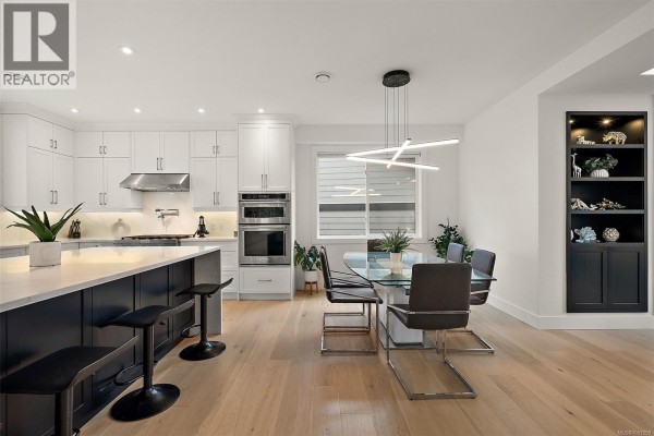 Kitchen island with seating, dining area, and black built-in shelving unit. - 4257 Pullet Pl, Saanich