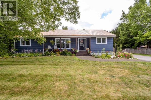 Exterior of a blue house with a tan metal roof, surrounded by greenery and a lawn. - 426 Granville Street E, Bridgetown