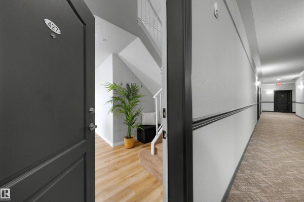 Apartment entrance door A427 opens to a small hallway with stairs and a potted plant. - #427 3425 19 St Nw, Edmonton