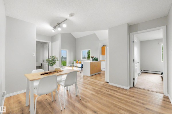 Dining area with light wood table and white chairs, leading into the living room and kitchen. - #427 3425 19 St Nw, Edmonton