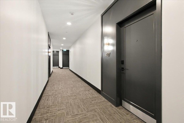 Long apartment building hallway with patterned carpet, recessed lighting, and dark gray doors. - #427 7463 May Cm Nw, Edmonton