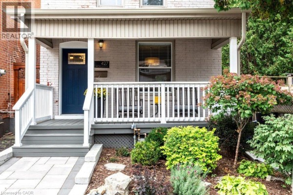 Close-up of the covered front porch showing the navy blue front door and seating area. - 427 Jackson Street W, Hamilton